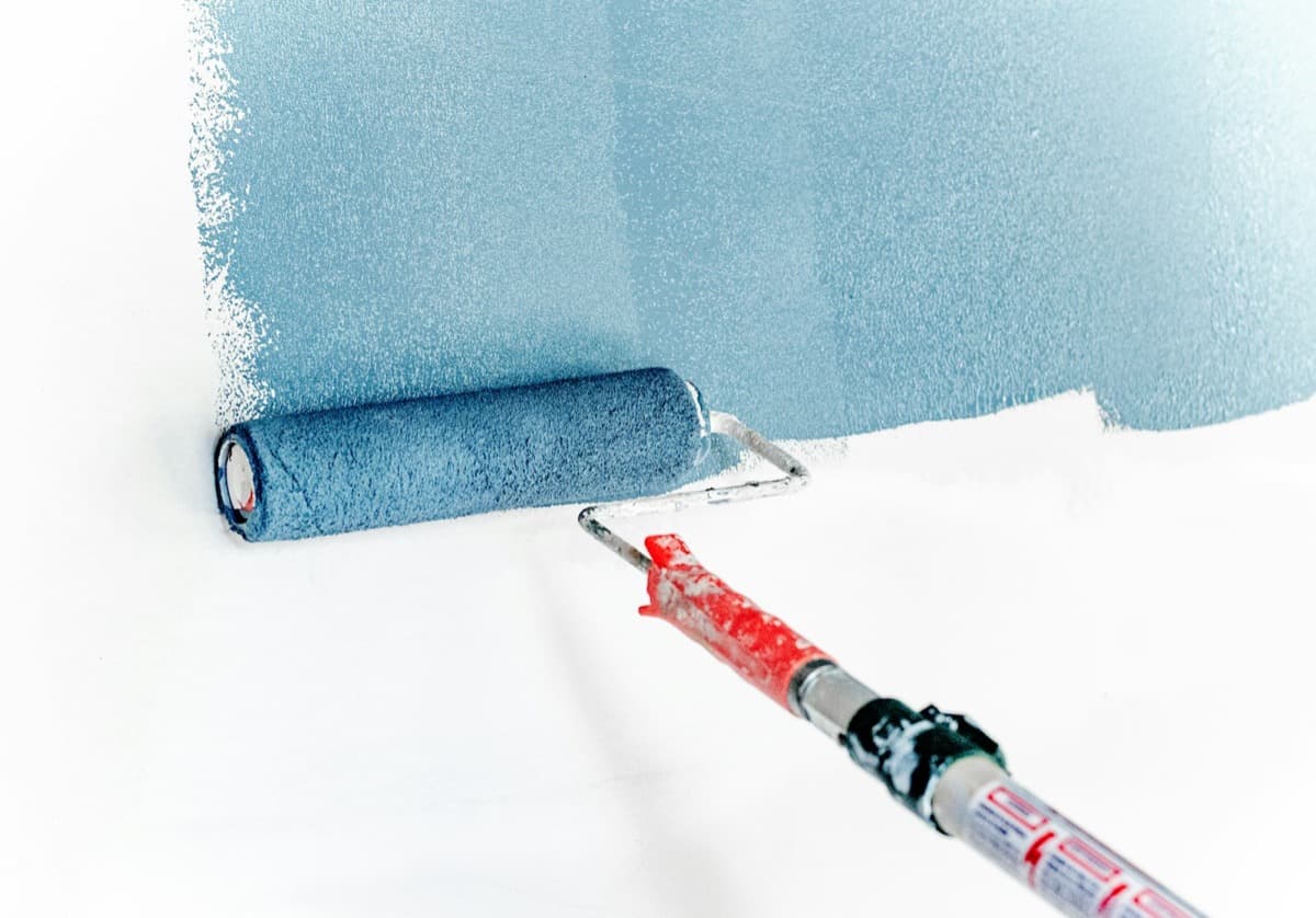 Roller laying down a coat of blue paint on a white wall