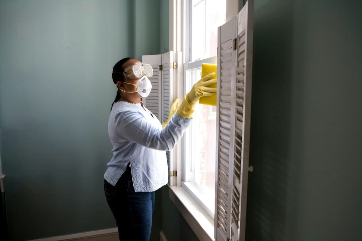 Woman in gloves cleaning and prepping window shutters