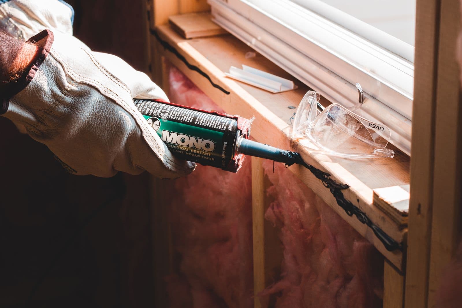 Gloved hand running a bead of caulk along a window frame