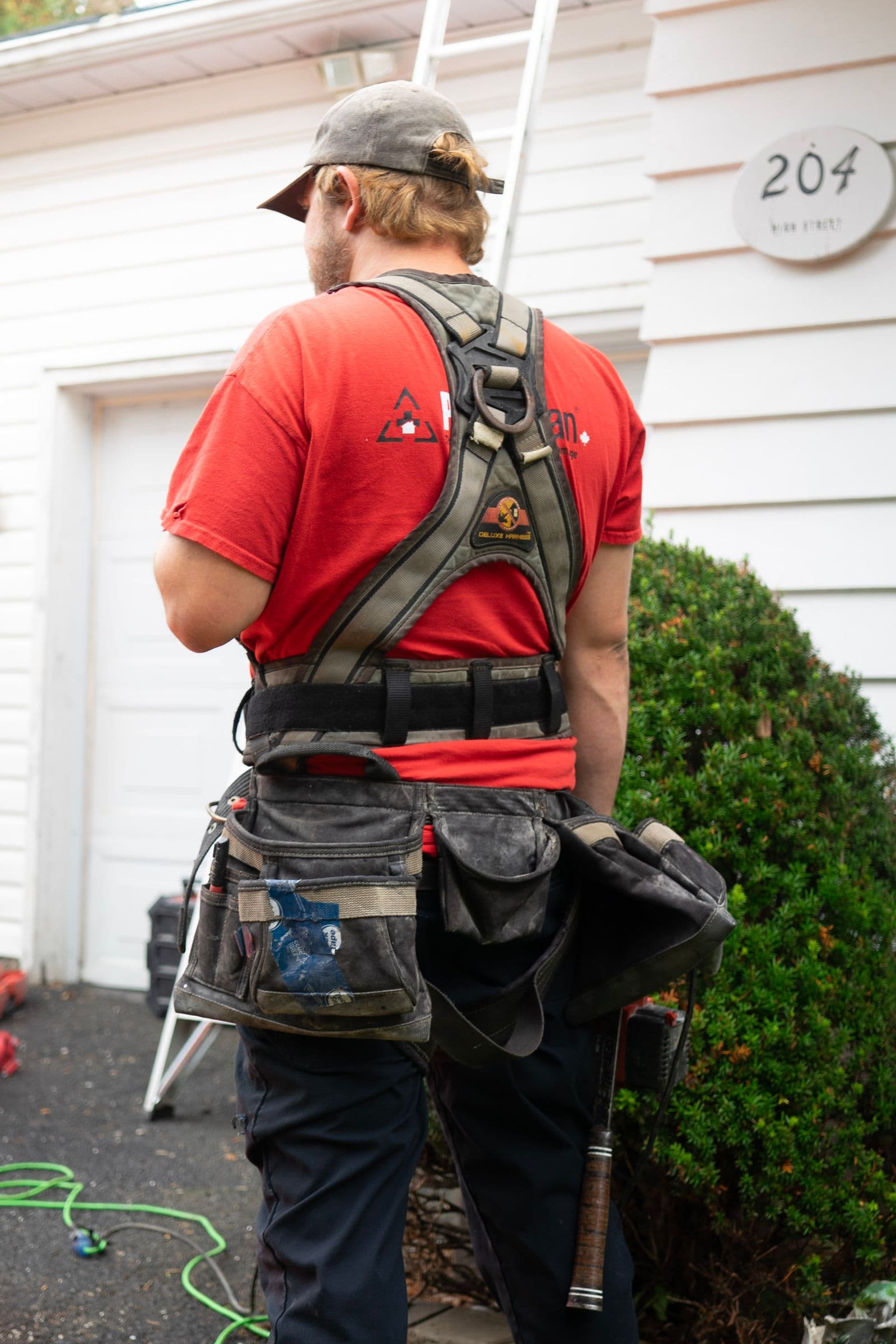 Crew member in a tool harness beside a white-sided house