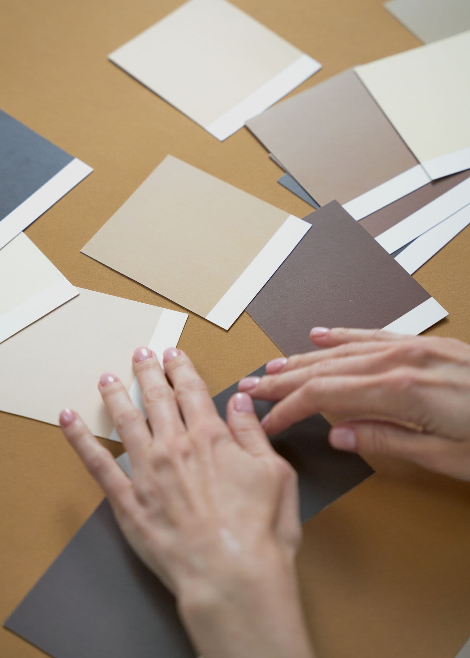 Hands arranging neutral paint swatches on a table