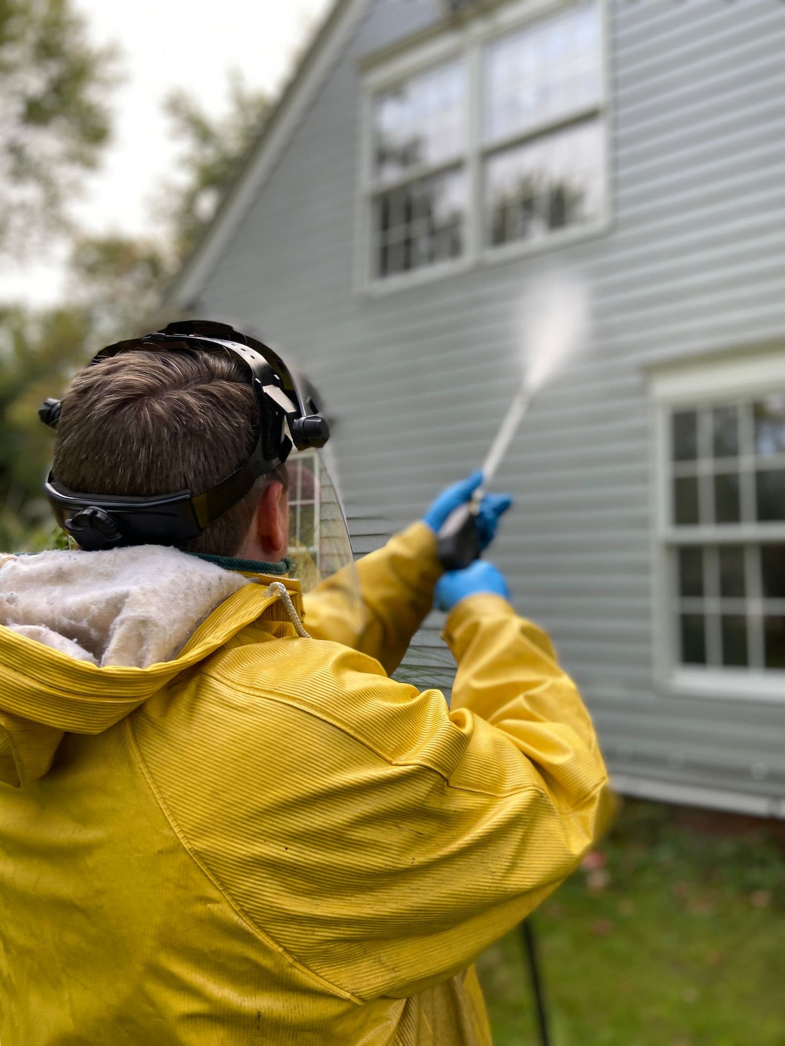 Painter in a rain jacket pressure washing a home's siding