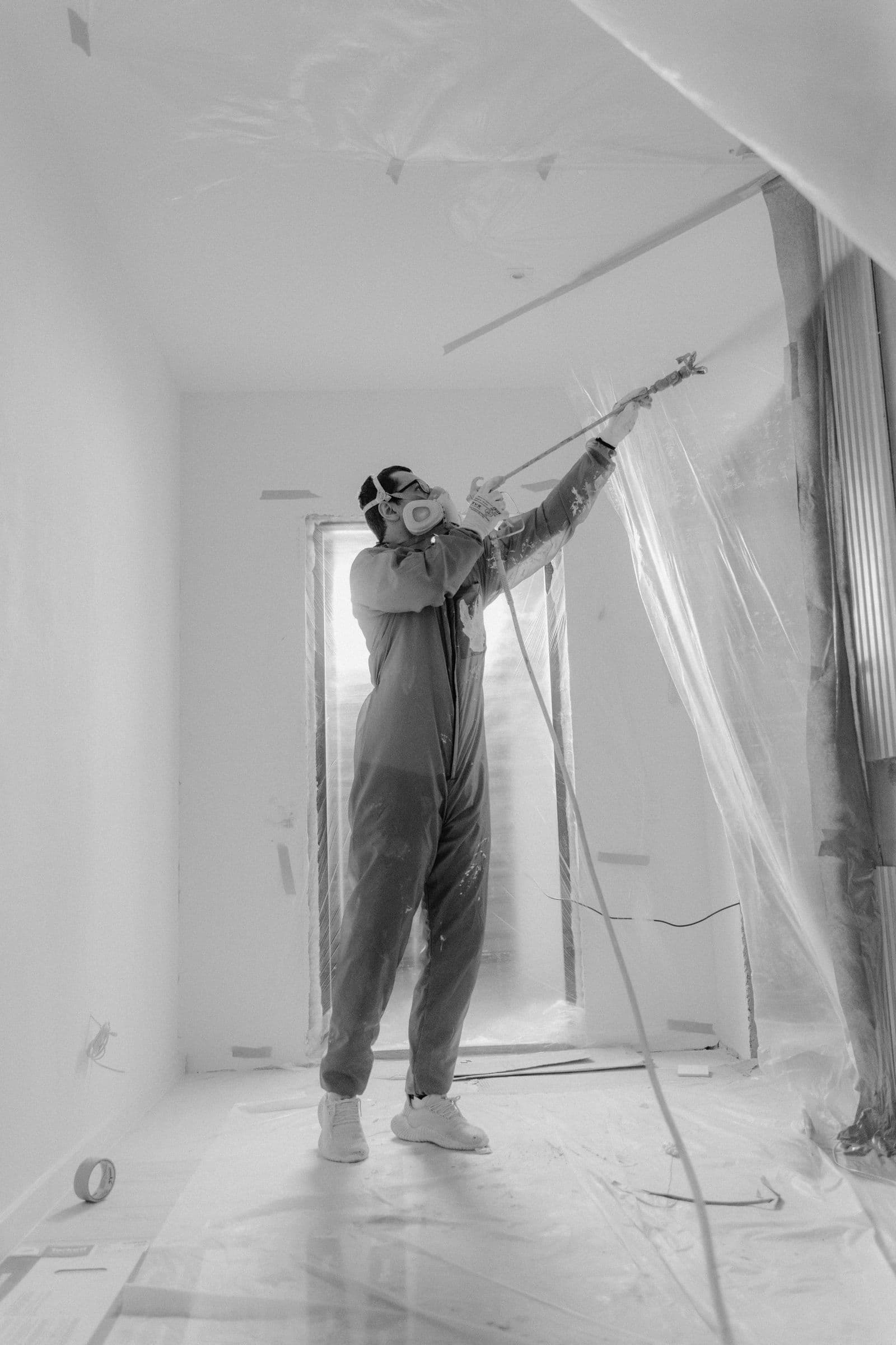 Painter in a respirator spraying inside a room sealed with plastic