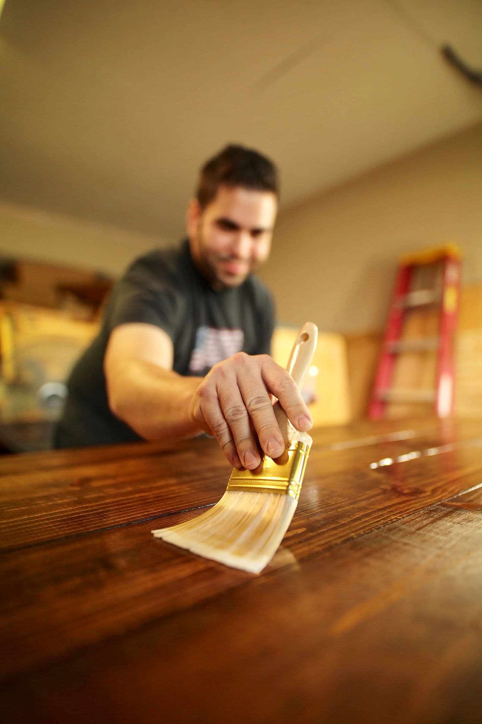 Painter brushing stain onto bare wood