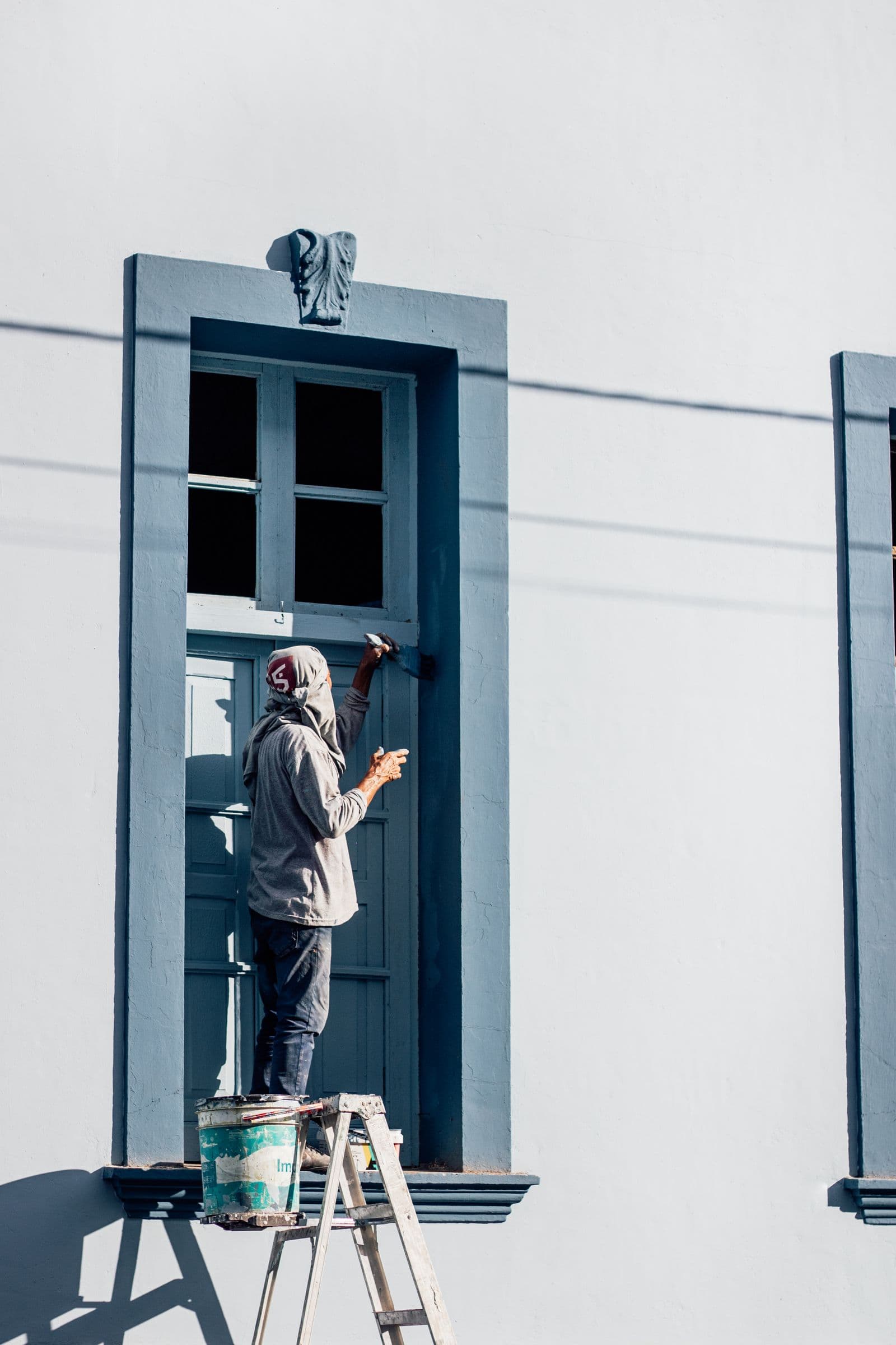 Painter on a ladder brushing a window frame